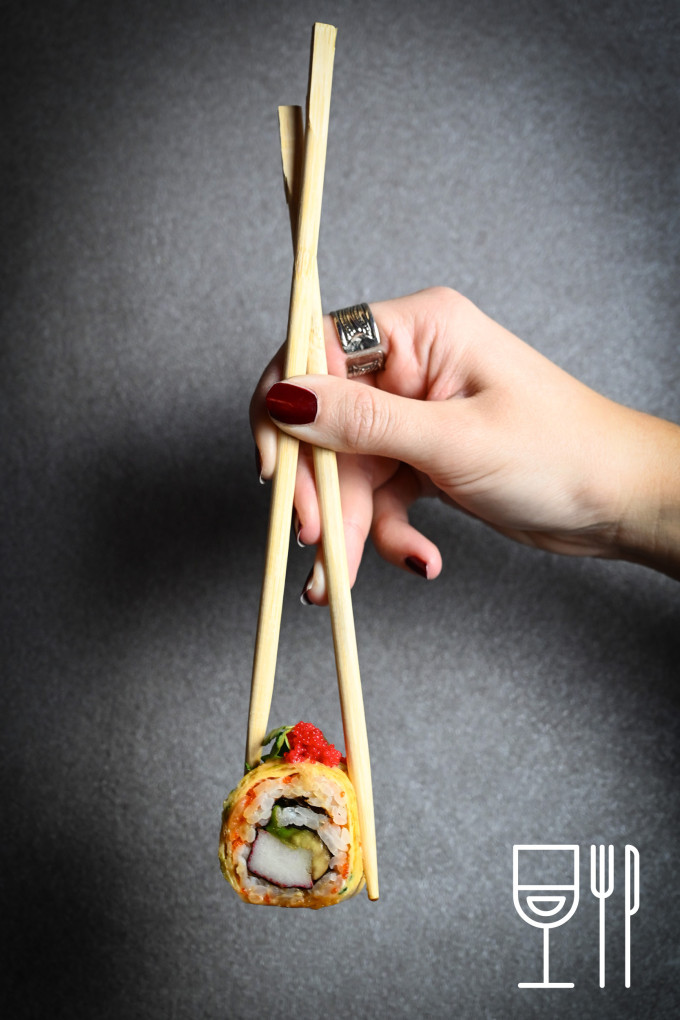 eine Hand, die Essstäbchen mit Sushi hält
